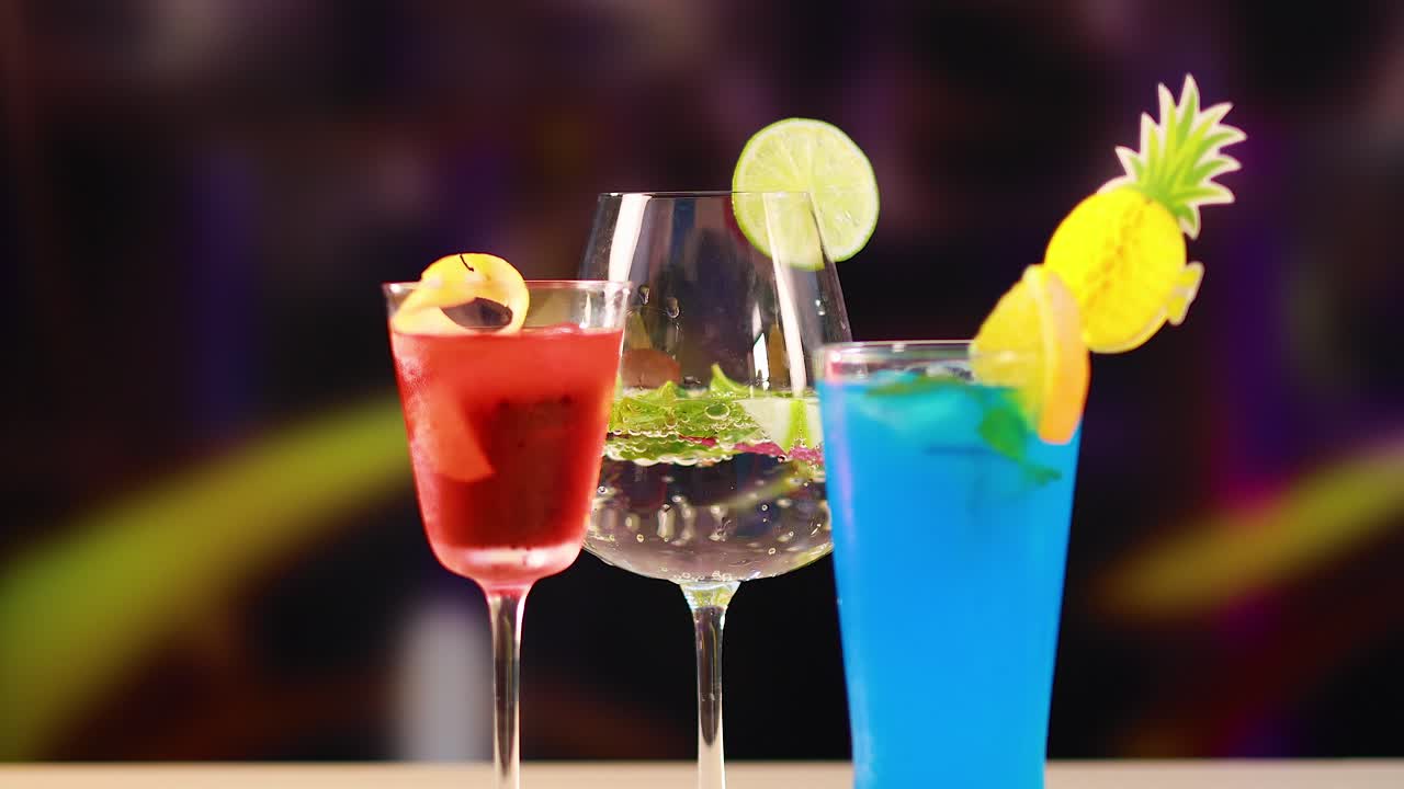 Three cocktails with vibrant garnishes in a lively bar environment, highlighting colorful drinks and festive atmosphere