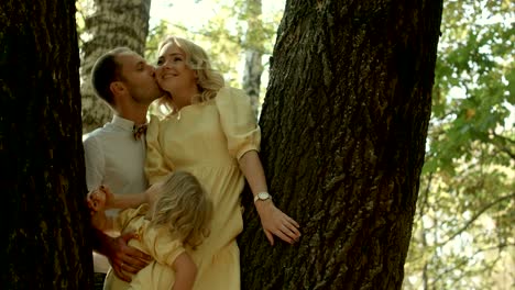 happy couple with her little daughter kissing over a forest background