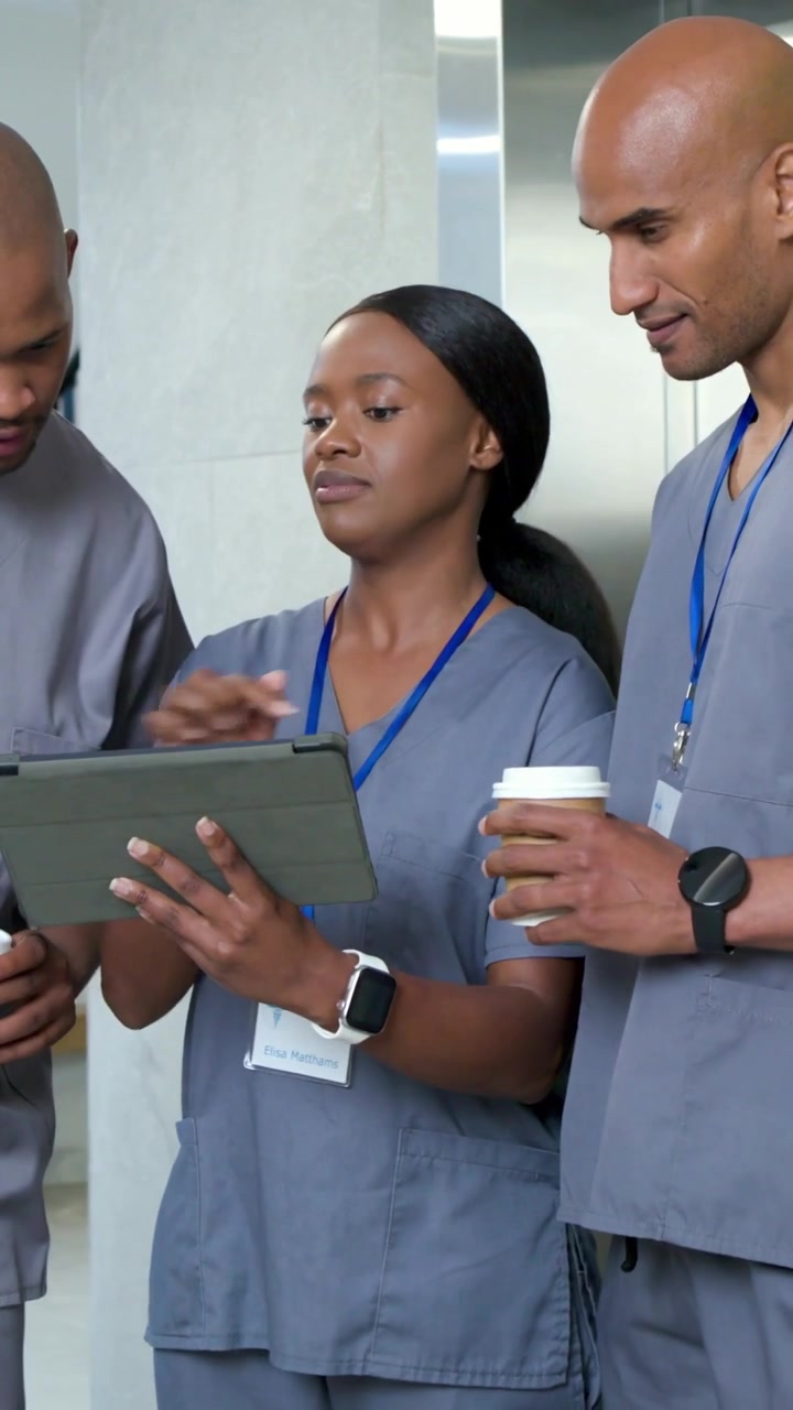 Vertical video: Tapping nurse in scrubs showing tablet near lift after cue man with cup reviewing