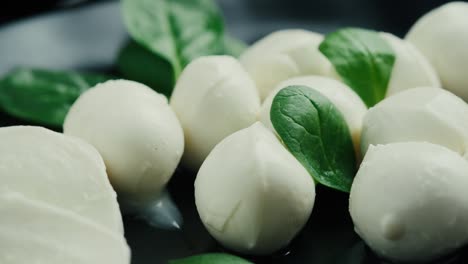 white small mozzarella cheese balls, spinach leaves on black plate. rotaiting shot