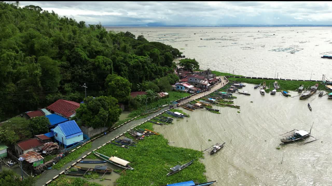 Pemandangan udara menunjukkan parkir perahu nelayan, jalan pesisir, rumah-rumah desa, dan ombak berkilauan dalam cahaya keemasan di atas air terbuka Ithan, Kalinawan, Bingnagonan, Rizal, Filipina.