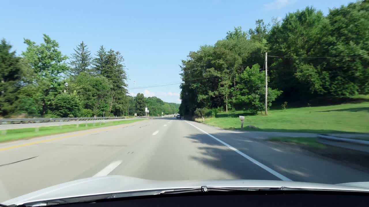 A quiet countryside road bordered by lush green trees and a bright blue sky. Perfect for a scenic drive, this peaceful landscape offers a glimpse of nature's calm beauty.