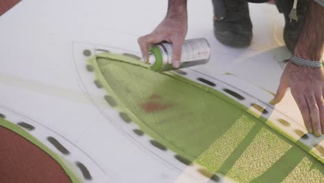 A person is using spray paint to add green color to a design, part of a creative process