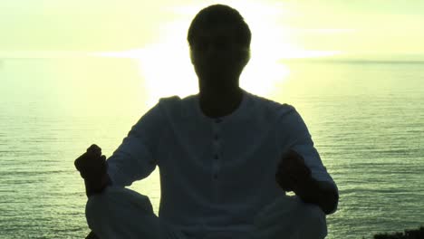 man practicing yoga by the ocean