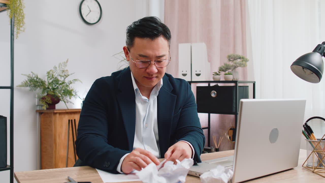 Angry furious man working at home office throwing crumpled paper having nervous breakdown at work