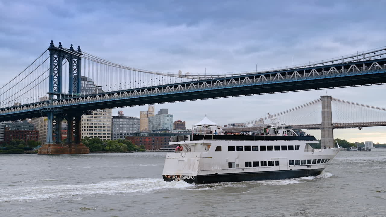 Modern cruise boats move under the Manhattan Bridge in New York, USA. River tour by the East River on a grey day
