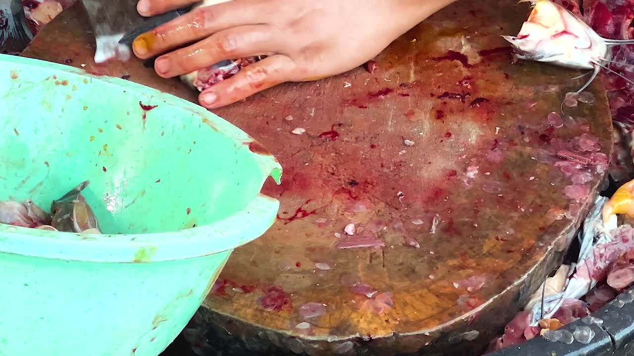 Close-up of fish pieces being cut on a wooden board beside a green basin.