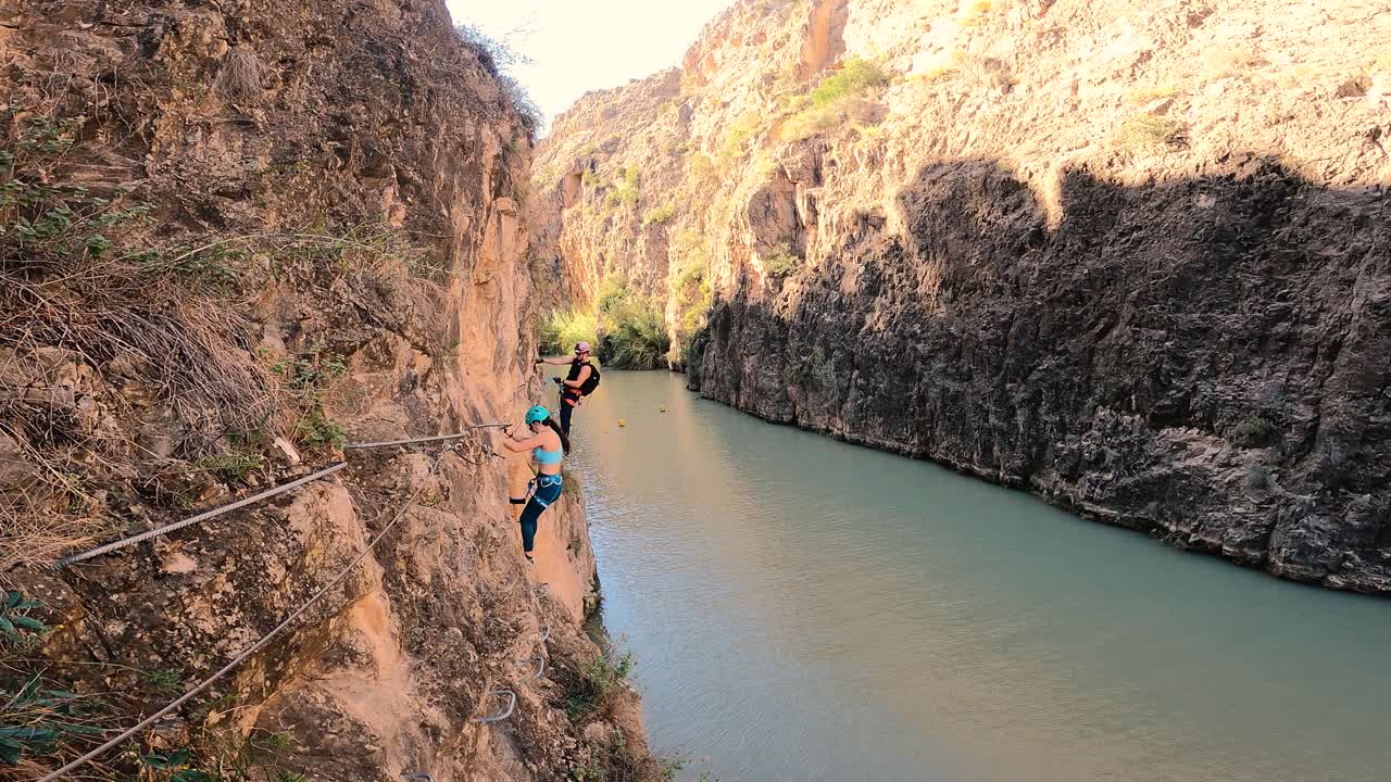 Couple doing via ferrata in Almadenes Canon, Cieza. Risky rock climbing above river in Spain.