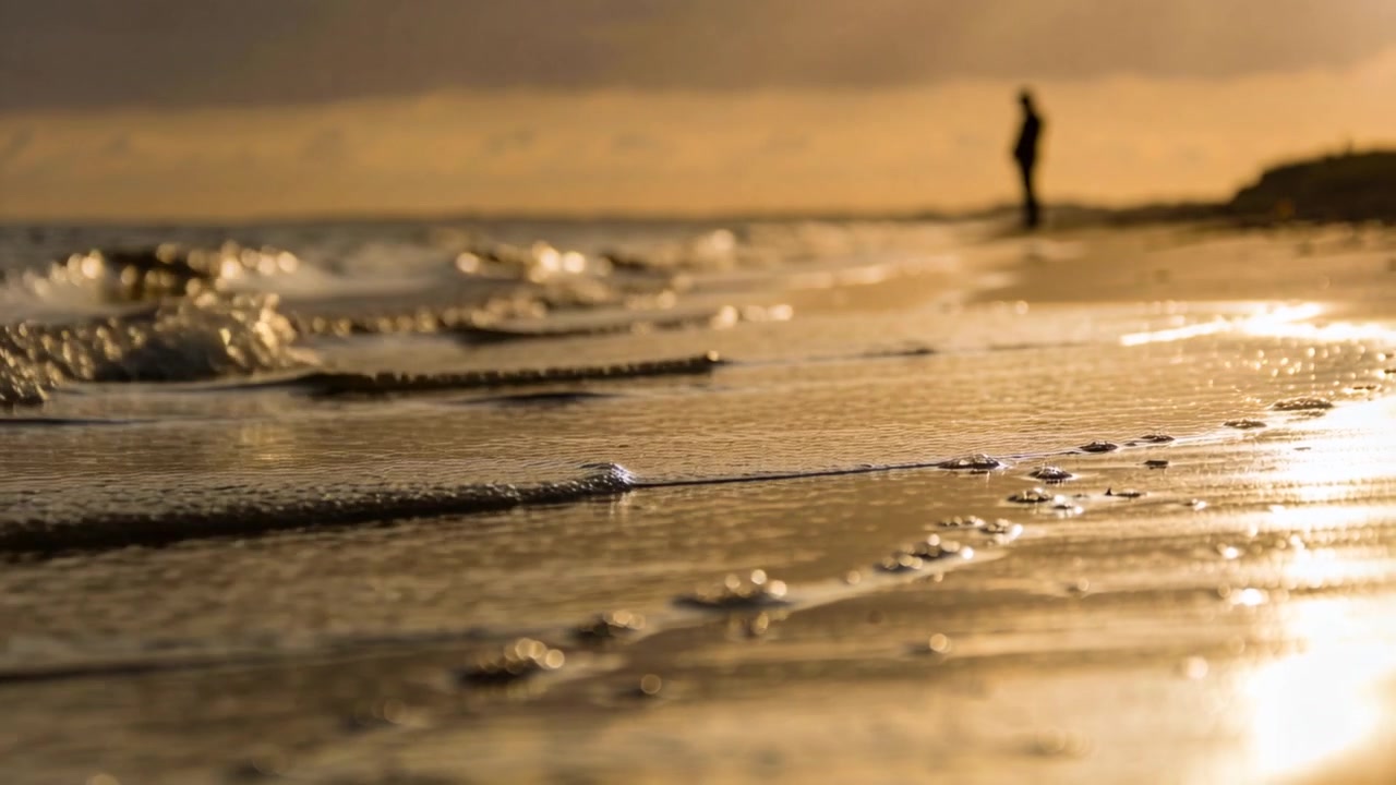 Onde in arrivo che rotolano sulla sabbia bagnata, una figura in abiti casual guarda il tramonto sulla destra, con spazio per il testo.