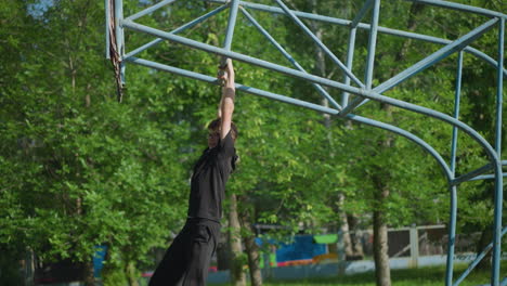 a young boy wearing a black outfit and glasses swings slowly on outdoor equipment, with lush green trees and a fence in the background