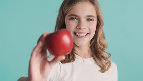 una adolescente caucásica en pijama sosteniendo una manzana y sonriendo.