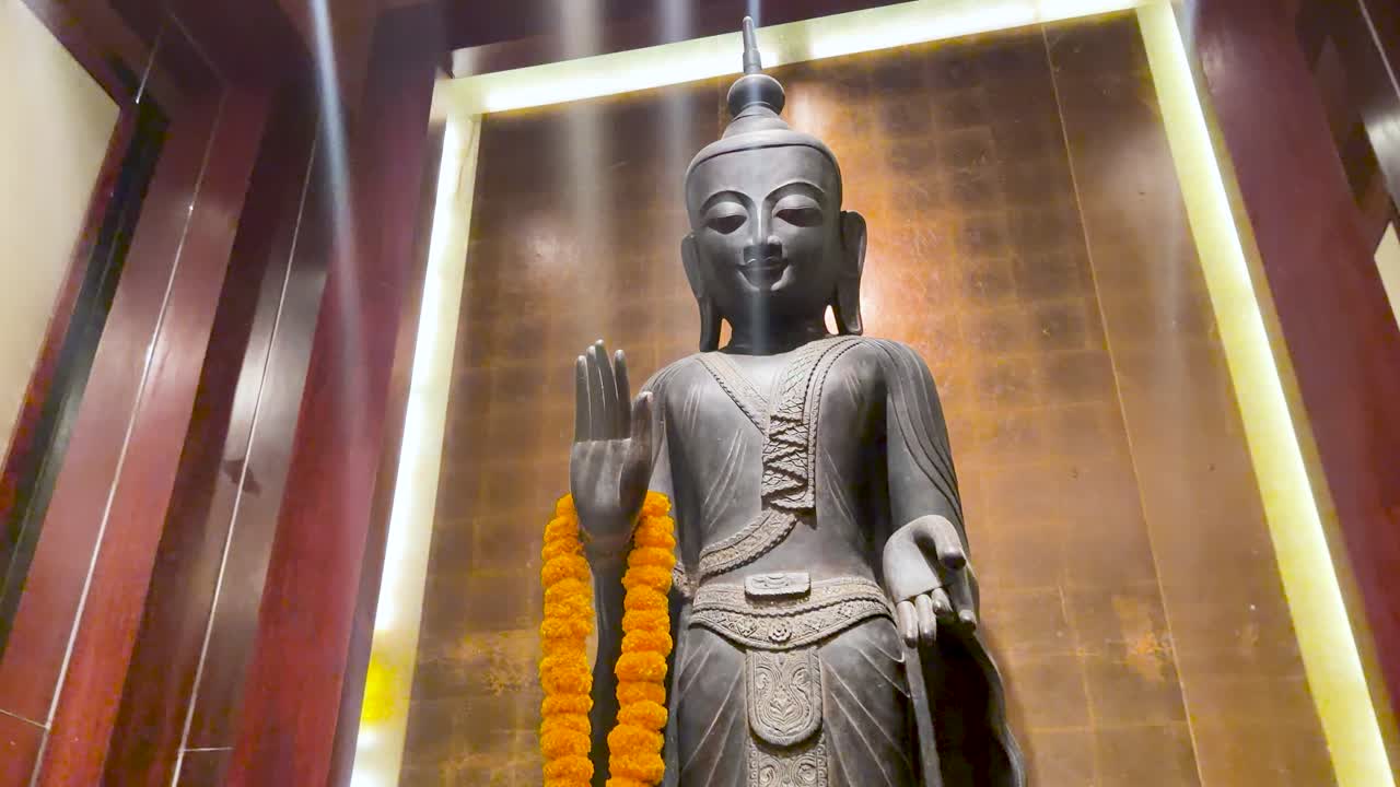 Inquadratura dal basso di una statua di Buddha in piedi con ghirlanda arancione nella sontuosa hall di un hotel