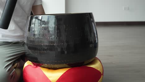 Man-Crouching-On-Ground-Striking-Gently-Tibetan-Singing-Bowl-Using-Mallet