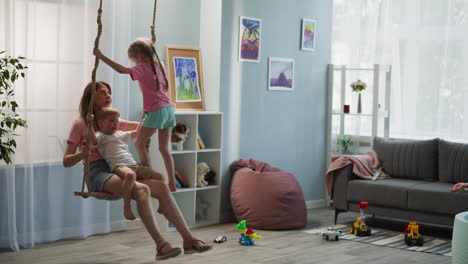 young mother sits on swing in room with sofa and toys