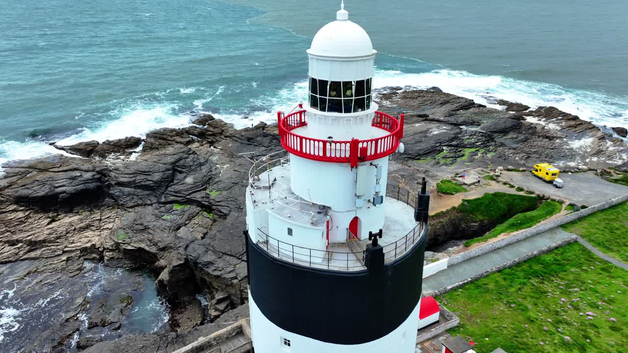 Ireland Epic Locations Hook Head Lighthouse Wexford drone closeup orbiting the top of the Lighthouse with tourists walking on it rocks below