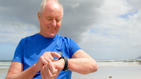 Vista-Frontal-Del-Anciano-Caucásico-Usando-Un-Reloj-Inteligente-En-La-Playa-4k