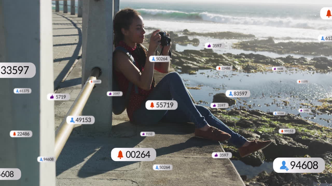 woman holding camera capturing ocean on seaside pier, with floating social media marketing icons