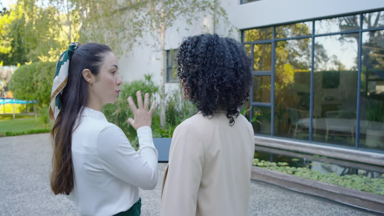 Donne diverse che arrivano a una casa, un agente con un tablet indica e spiega la facciata in vetro e lo stagno.