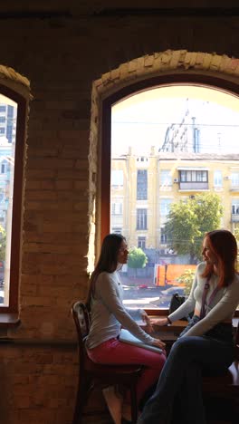 two young women having a conversation at a cafe near the window