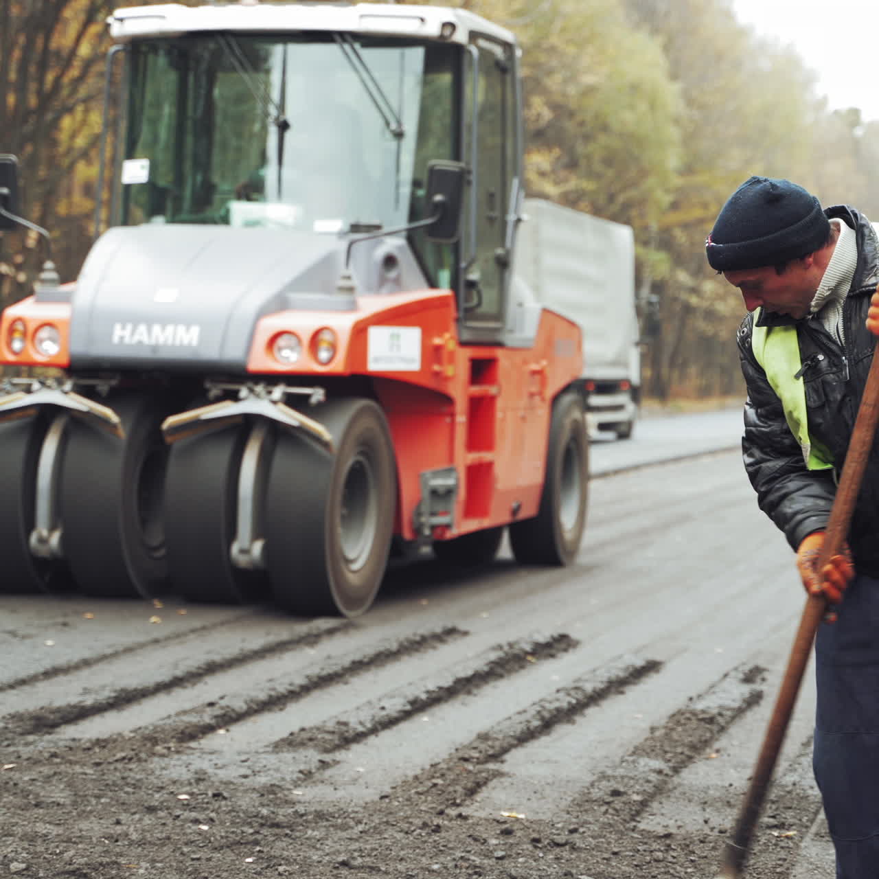 Workers in protective clothes with shovels working on the background of paver machines. New technics and team of workers making fresh asphalt. Street resurfacing.