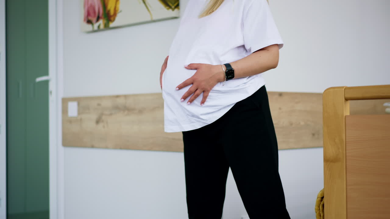 Pregnant woman with big belly before labor. Lady stands swaying from side to side and looks at watch to count time between contractions. Low angle view.