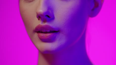 extreme close up of a young woman holding her finger to her lips to symbolize silence or being quiet in front of purple background in slow motion