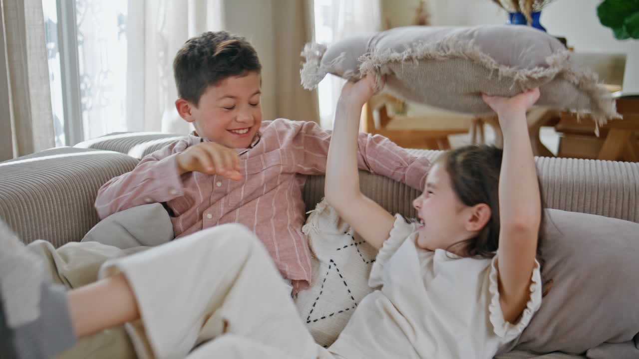 Funny kids pillows fighting at sofa closeup. Carefree little children having fun