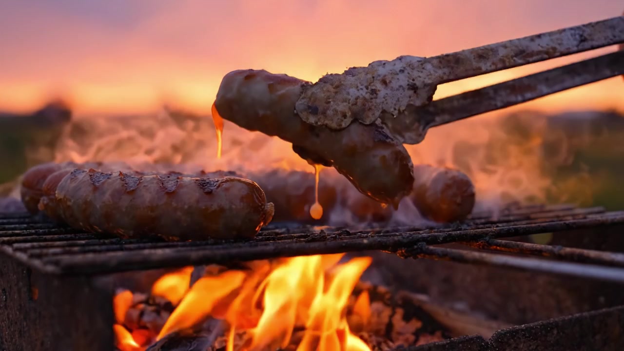 Sydende pølser grilles over en glødende grill ved solnedgang, der fanger glødernes varme skær og den rige aroma af perfekt tilberedt kød.