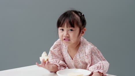 Asiatic-child-eating-piece-of-sweet-in-the-studio-with-a-gray-background