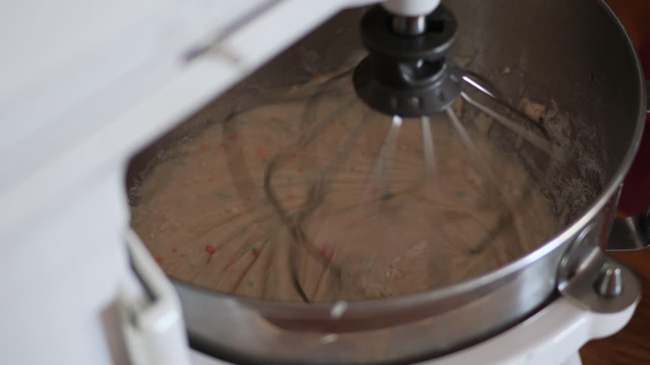 la masa del pastel de funfetti se batía juntos en un cuenco de mezcla de cocina de metal en la encimera mientras alguien acelera y ralentiza hasta detenerse las velocidades de batido