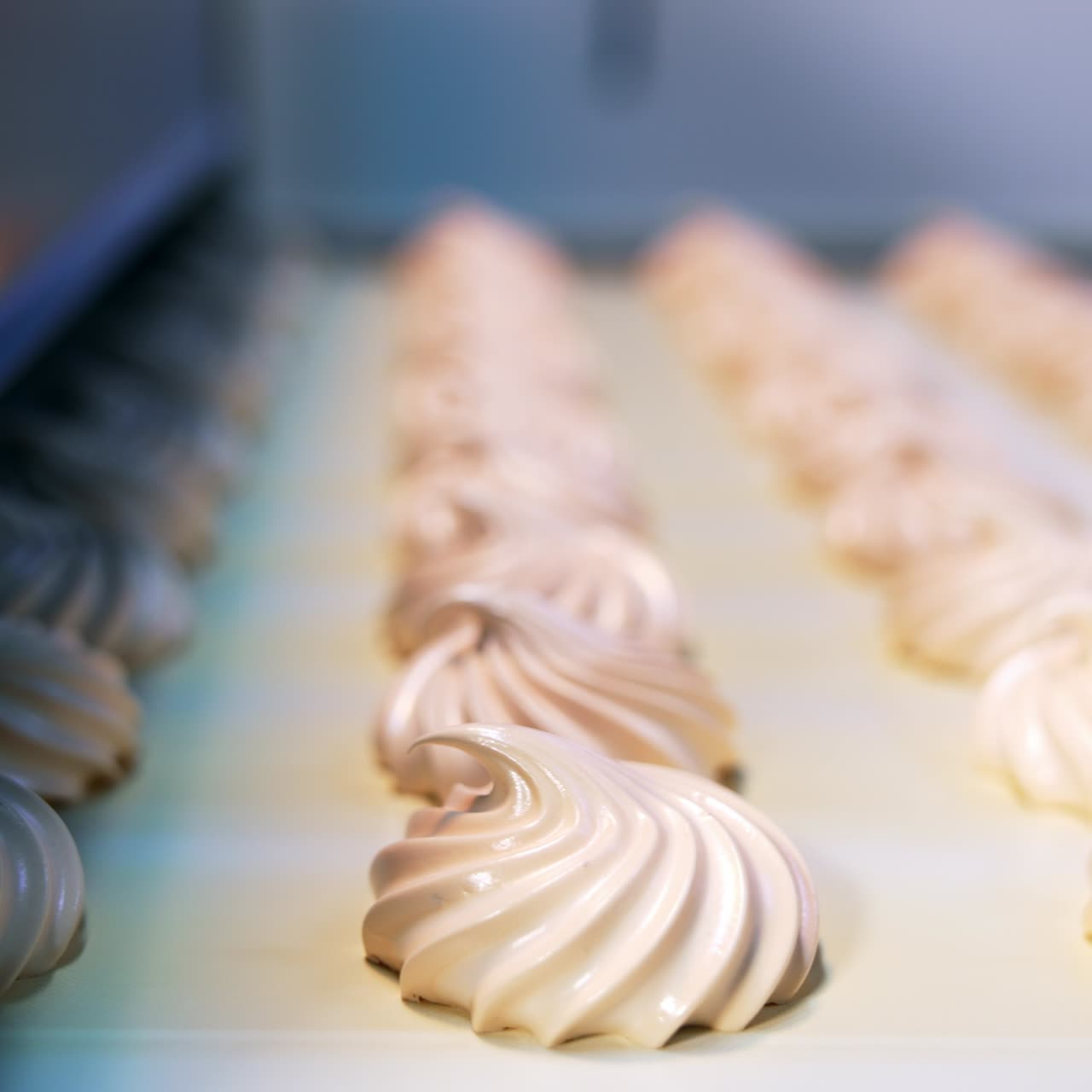 Yummy creamy desserts come out from the machine at confectionery. Freshly-laid zephyr sweets on the conveyor line. Close up. Blurred background