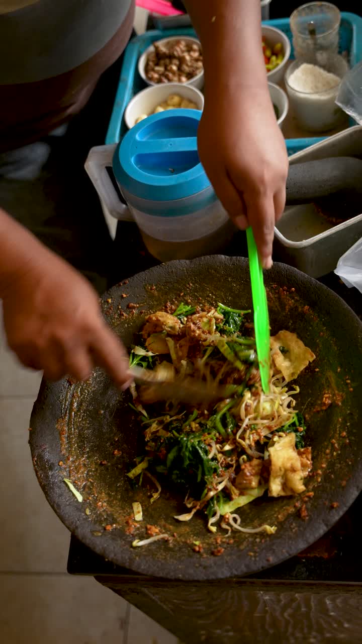 Vertical close-up of traditional Javanese lotek kupat dish being prepared with vegetables, rice cake, and peanut sauce, a popular Indonesian street food specialty