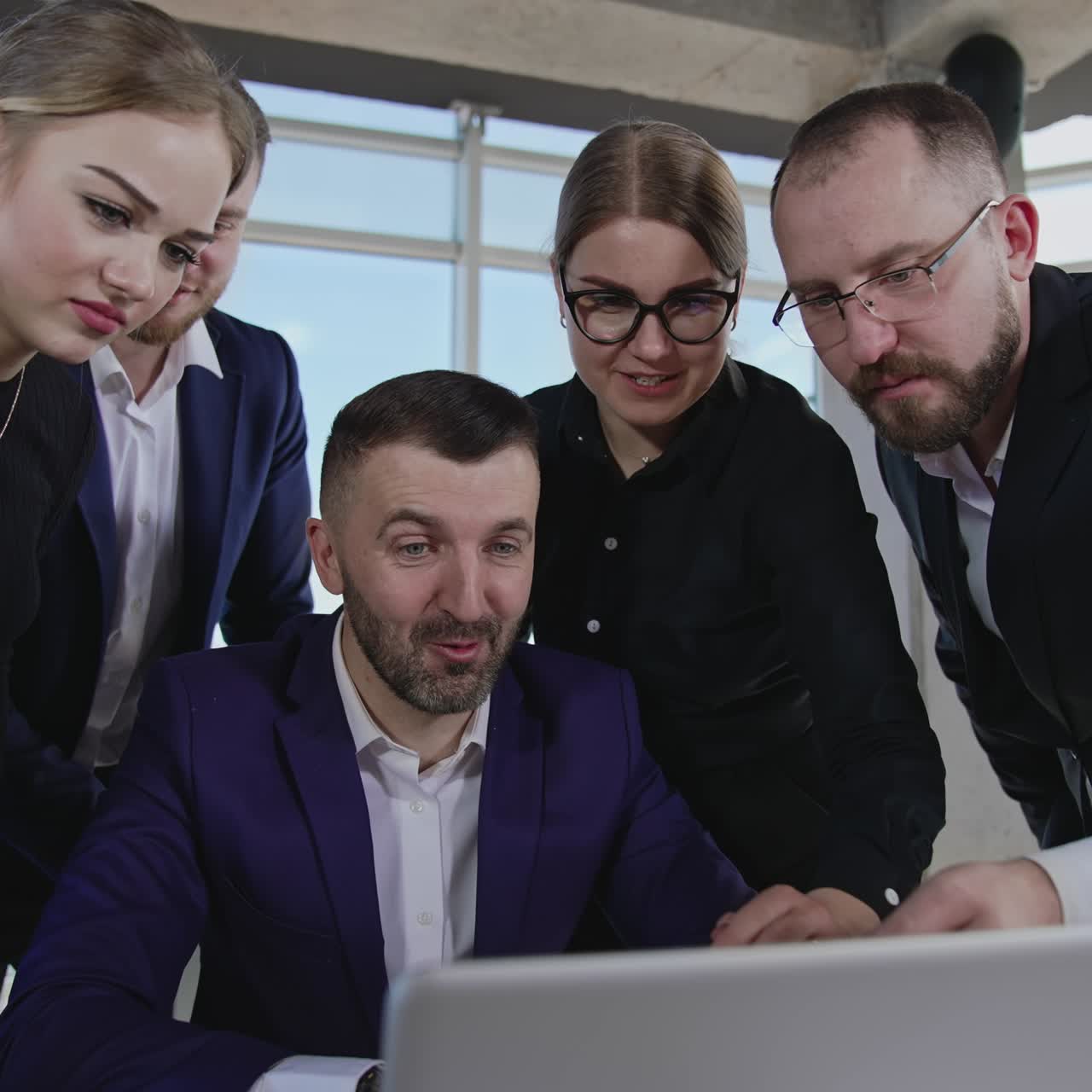Colleagues gathered around laptop. Workmates point at the computer and discuss their working issues. Gradual close up to the coworkers