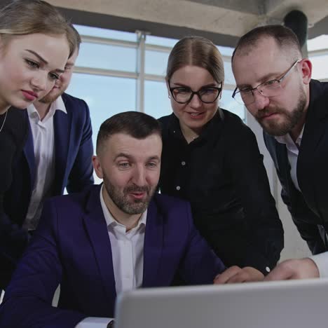 colleagues gathered around laptop. workmates point at the computer and discuss their working issues. gradual close up to the coworkers