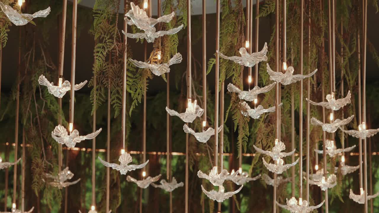 hanging glass dove ornaments with integrated candle lights amid greenery and wooden rods