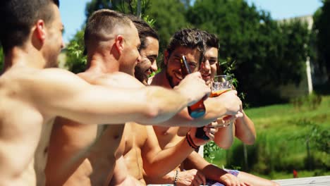 Group-of-friends-toasting-drinks-while-sitting-on-the-edge-of-pool-