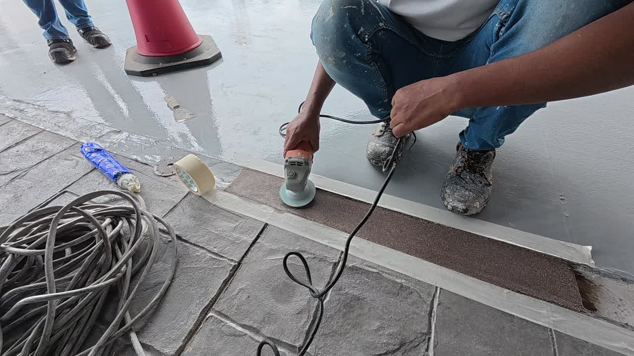 Uneven concrete patching is being ground smooth by a construction worker using an electric grinder. Safety is the top priority for this meticulous work.