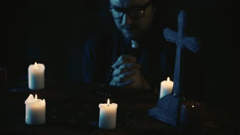video capturing a table with magical tools on it a priest is sitting at the table with beads in his - video capturing a table with magical tools on it. a priest is sitting at the table with beads in his hands, praying with his eyes closed, when a hand lays on his shoulder. creative content, hallowee