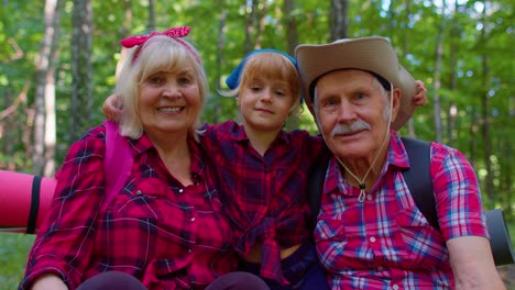 Active-senior-grandmother-grandfather-tourists-sitting,-hiking-with-granddaughter-in-summer-wood