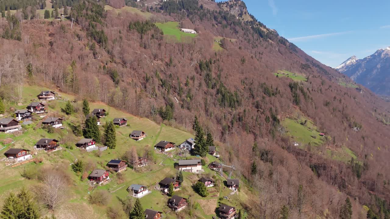 Alpejska osada Schlattberg nad Luchsingen z tradycyjnymi chatami na zboczu wzgórza i doliną Glarus w oddali. W tle widoczne ośnieżone góry. Ujęcie z drona