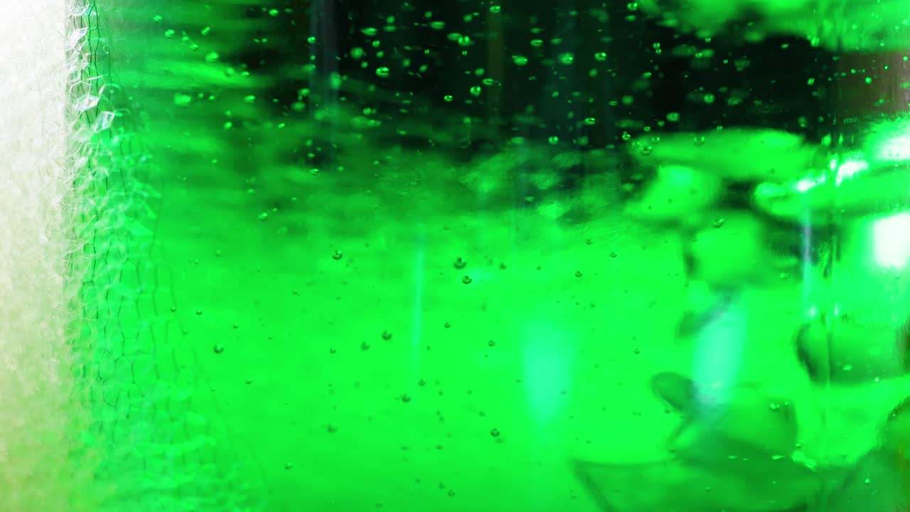 un líquido verde vibrante con burbujas se forma a medida que el hielo seco interactúa, creando un efecto visual dinámico en un entorno controlado