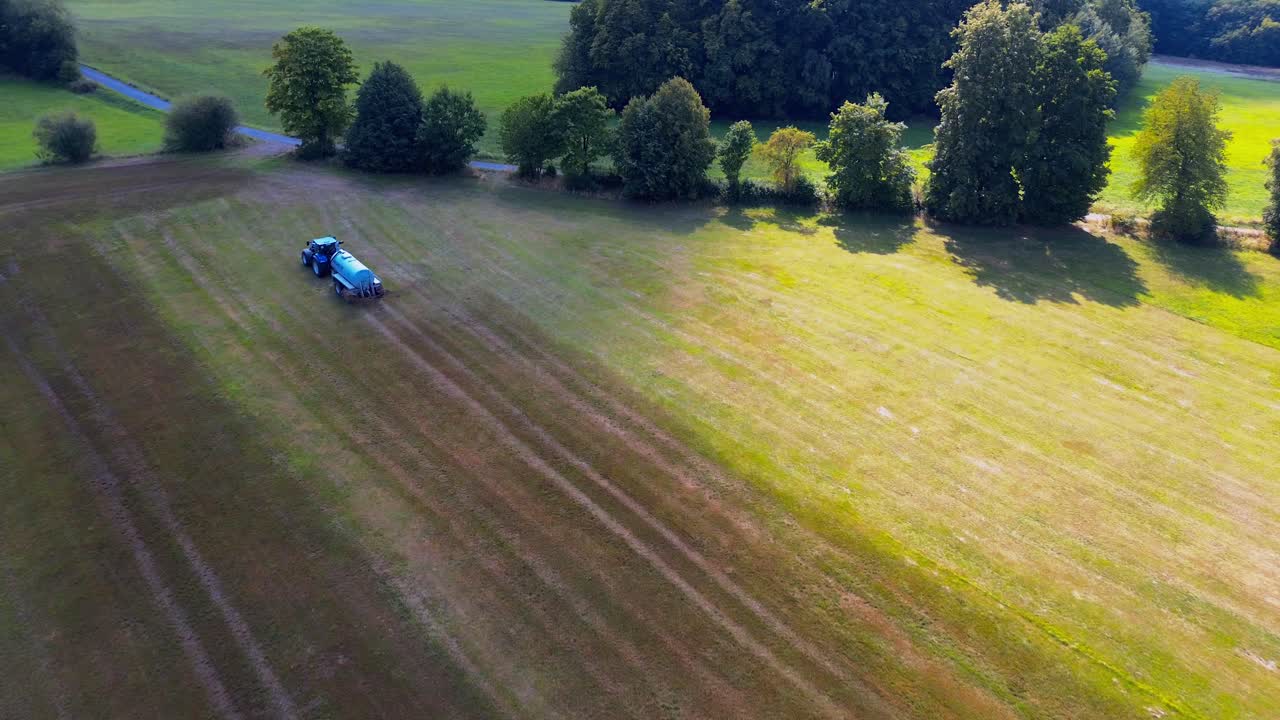 Aerial View of Blue Tractor Spraying Crop Field with Agricultural Machinery on Sunny Day