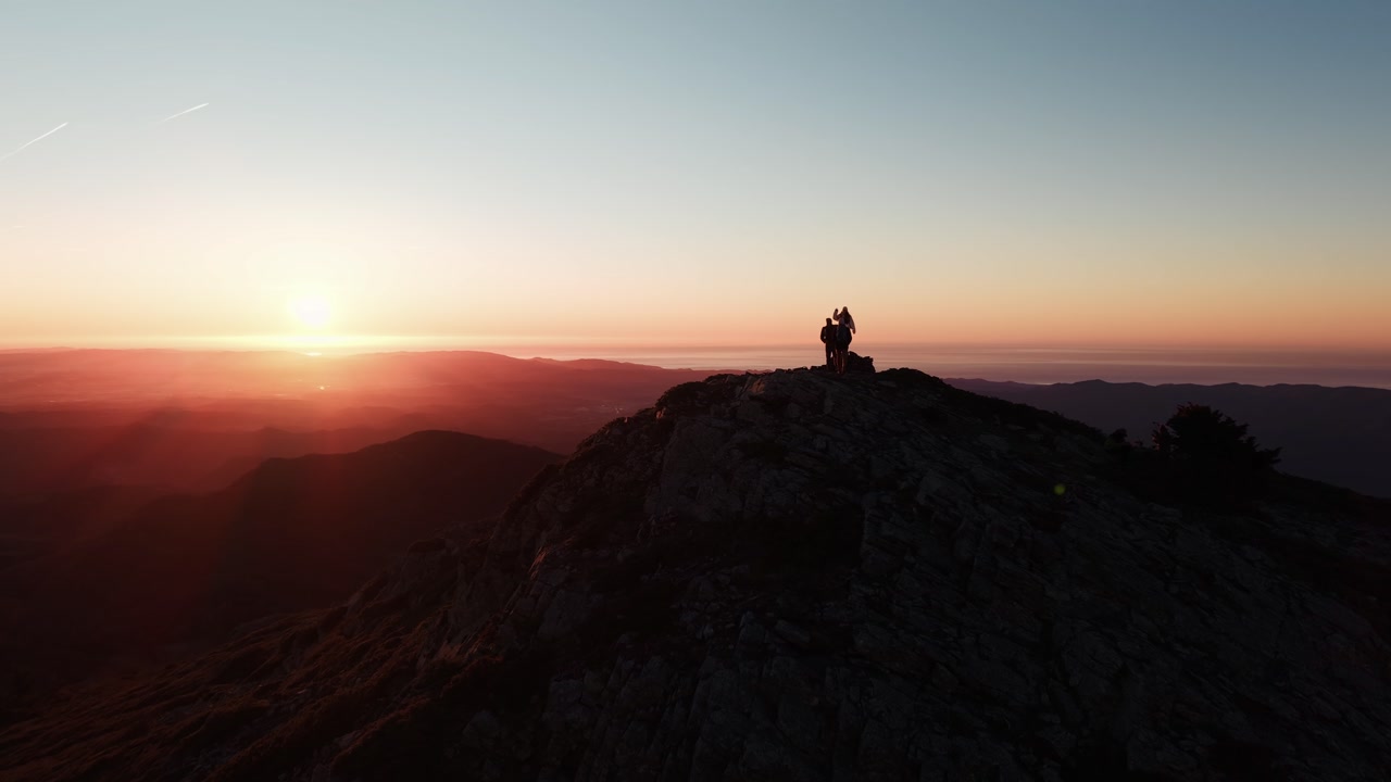 Drone approaches hikers silhouettes at sunrise on Turó de l’Home Montseny summit