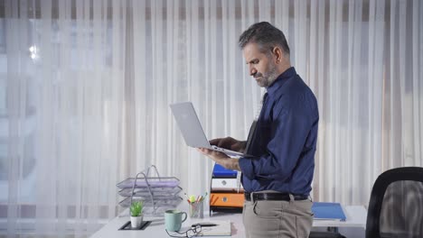 Thoughtful-mature-businessman-standing-working-at-laptop,-typing-on-keyboard.