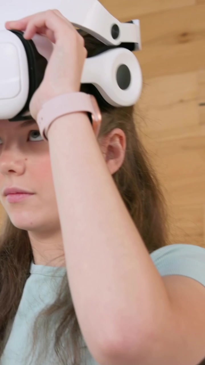 Vertical video: Tapping gray tablet on bed, woman in mint tee donning white headset to view content