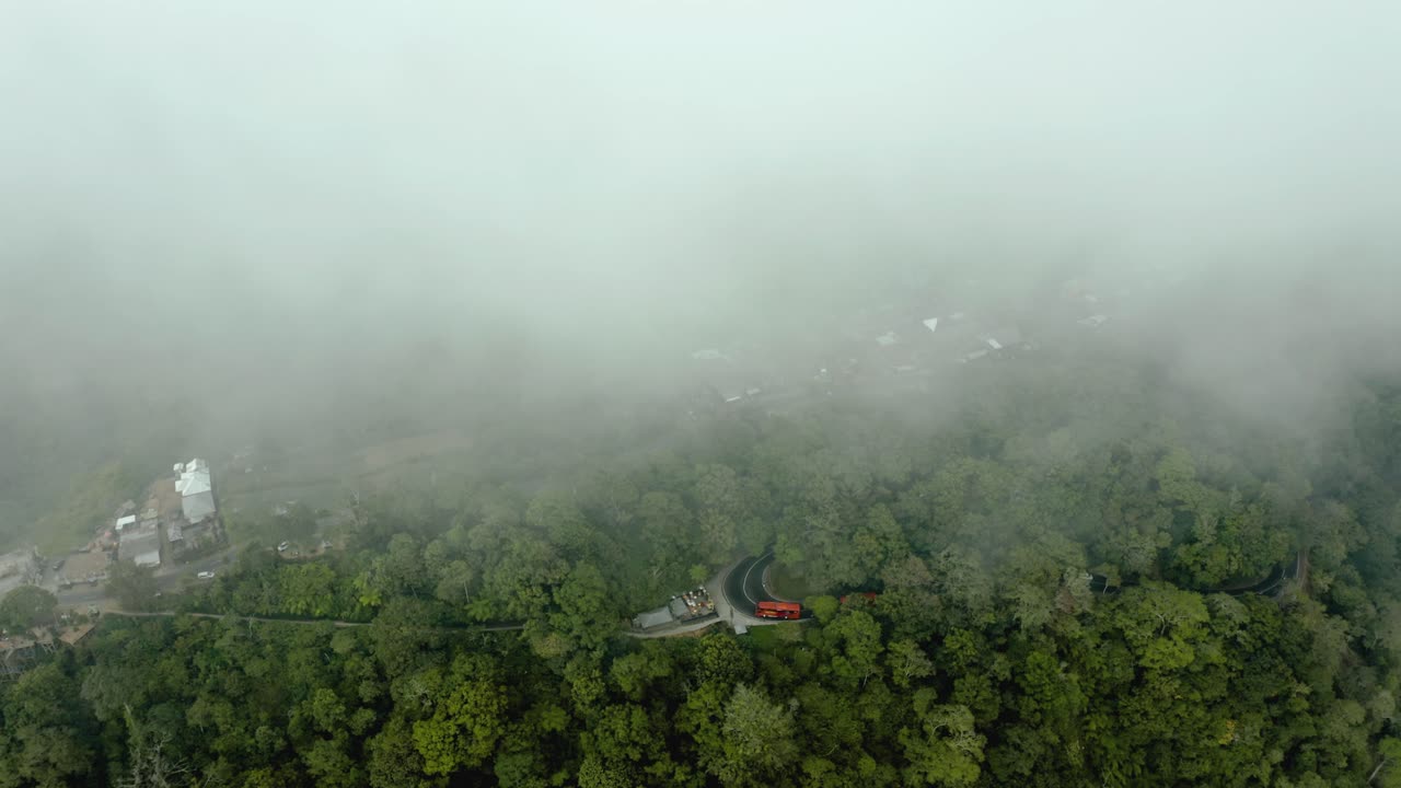 An aerial shot of a bus going through a jungle road which then fades away as the drone flies into a cloud