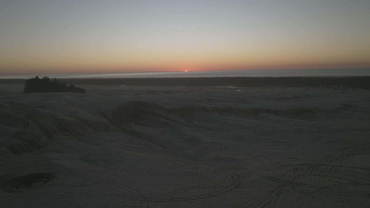 Slow aerial pullout looking towards sunset, flying low over sand dunes of Dunes City, Oregon, near Florence.