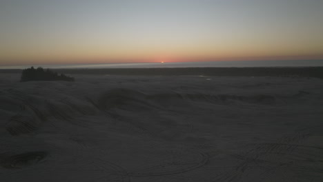 slow aerial pullout looking towards sunset, flying low over sand dunes of dunes city, oregon, near florence.