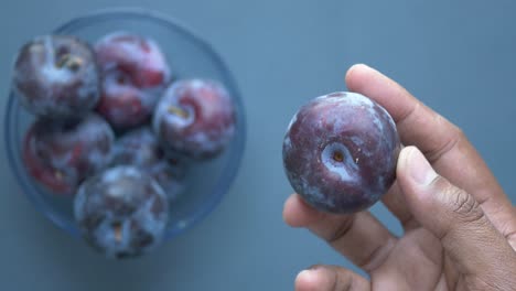 hand holding a plum, with other plums in a bowl