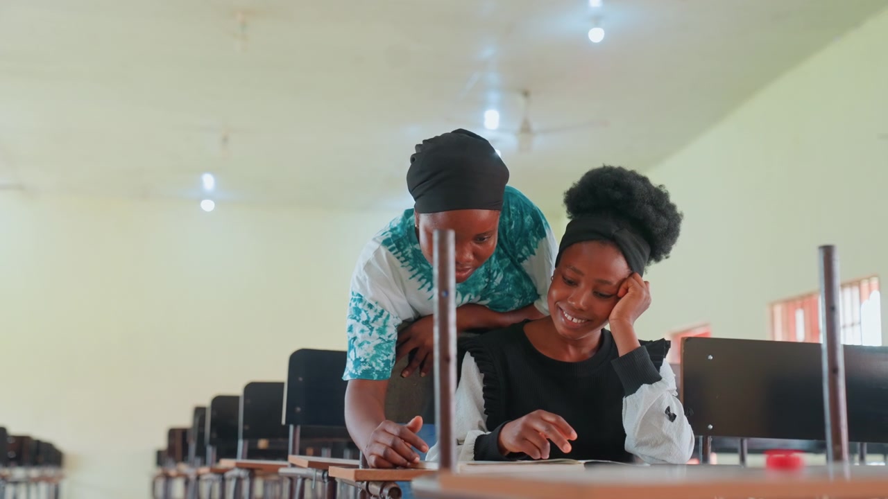 Black mother comforting daughter at computer. Mother leans over shoulder with gentle embrace, daughter smiles while studying, monitor and notebooks on desk, warm lighting and nurturing support